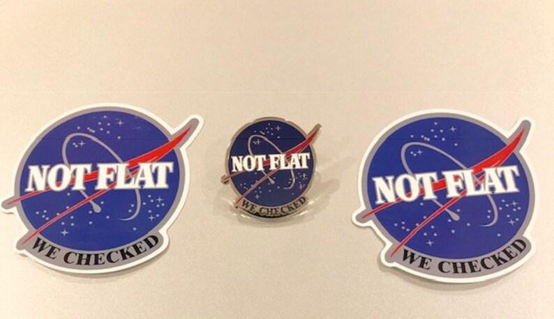 May include: Three stickers with a blue and white NASA-style logo that says "NOT FLAT WE CHECKED" in white letters. The stickers are in different sizes and one is a pin.