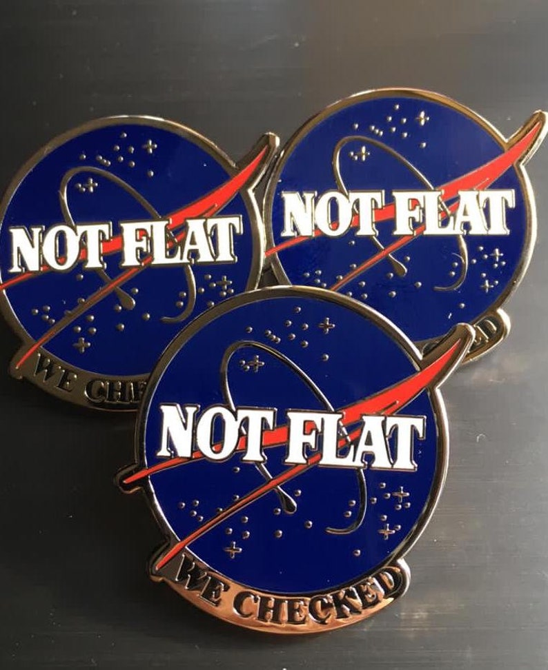 May include: Three gold-colored pins with a blue and red NASA-inspired design. Each pin features the text "NOT FLAT" and "WE CHECKED" in white lettering.