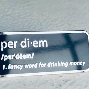May include: A silver metal pin with the word "per diem" and the phonetic spelling "/pərˈdiːəm/" and the definition "1. fancy word for drinking money".