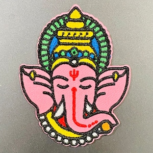 May include: A pink embroidered patch of a Hindu deity with a colorful crown and a third eye. The deity has a trunk and tusks, and is wearing a necklace with a yellow and black design.