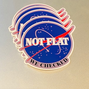 May include: A set of five stickers featuring a blue and white NASA-inspired logo with the text "NOT FLAT WE CHECKED" in red and white lettering.