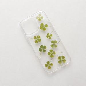 Può includere: Una cover trasparente per smartphone con un motivo sparso di quadrifogli pressati in tonalità di verde. La cover presenta un ritaglio rettangolare per il modulo fotocamera e ha una finitura liscia e lucida su tutta la superficie.