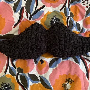 Peut inclure: Un oreiller en forme de moustache crocheté noir sur un fond blanc à motif floral.