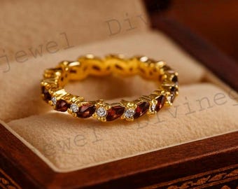 May include: A gold-colored ring with alternating red and white gemstones, displayed inside a wooden jewelry box. The ring features a continuous band of oval-shaped red stones and smaller, round white stones.