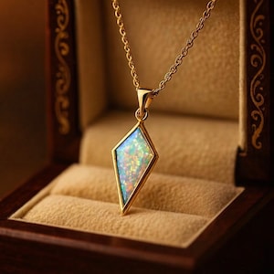 May include: A gold necklace featuring a diamond-shaped pendant with an iridescent opal gemstone. The necklace is presented in a dark wooden jewellery box with gold detailing.