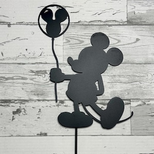 May include: Black metal silhouette of Mickey Mouse holding a balloon. The silhouette is attached to a metal stake.