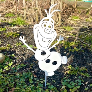 May include: White metal cutout of Olaf, a snowman character from the film Frozen, with a happy expression and outstretched arms. The cutout is attached to a metal stake for placement in the ground.