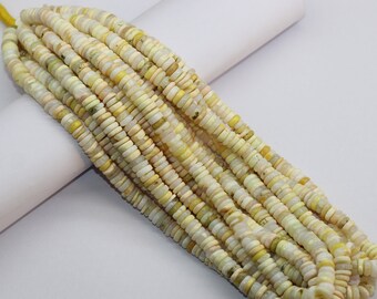 May include: A strand of small, flat, circular beads in shades of pale yellow, cream, and off-white. The beads are strung together on a thin yellow cord, creating a long, uniform row of smooth, disc-shaped pieces with a subtle, natural luster.