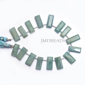 May include: A strand of 15 light blue aquamarine gemstone beads, each cut into a rectangular shape with faceted edges. The beads are strung on a silver wire and are approximately 1.5 cm long. The image includes the text "JMDBEADS".