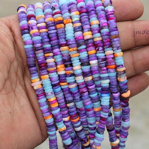 May include: A strand of colorful shell beads in shades of purple, blue, pink, and orange. The beads are small and round, and they are strung together on a clear thread. The beads are arranged in a random pattern, and they create a beautiful and eye-catching display.