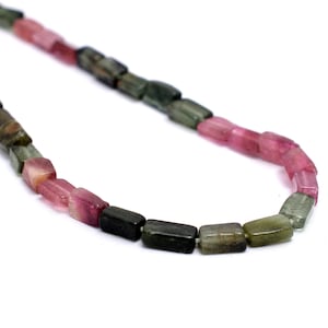 May include: A strand of green, pink, and black tourmaline beads. The beads are rectangular and faceted. The beads are strung on a clear thread.