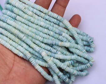 May include: A strand of light blue and white opal beads. The beads are small and round, and they are strung on a thin wire. The beads are arranged in a loose pile, and they are being held in a person's hand.