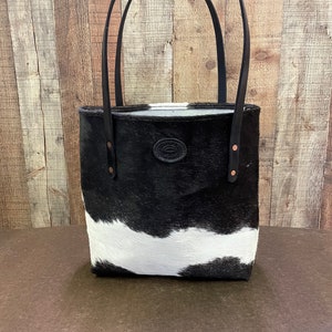 Pu&ograve; includere: Borsa tote in pelle di mucca bianca e nera con manici in pelle nera e un accento in pelle marrone. La borsa ha un design semplice ed &egrave; perfetta per l'uso quotidiano.