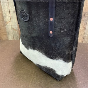 Pu&ograve; includere: Borsa tote in pelle di mucca bianca e nera con cinturini in pelle nera e una toppa in pelle marrone. La borsa ha una chiusura a zip ed &egrave; realizzata con materiali di alta qualit&agrave;.