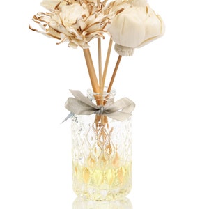May include: A clear glass bottle with a decorative pattern filled with a yellow liquid and wooden sticks topped with dried white flowers.