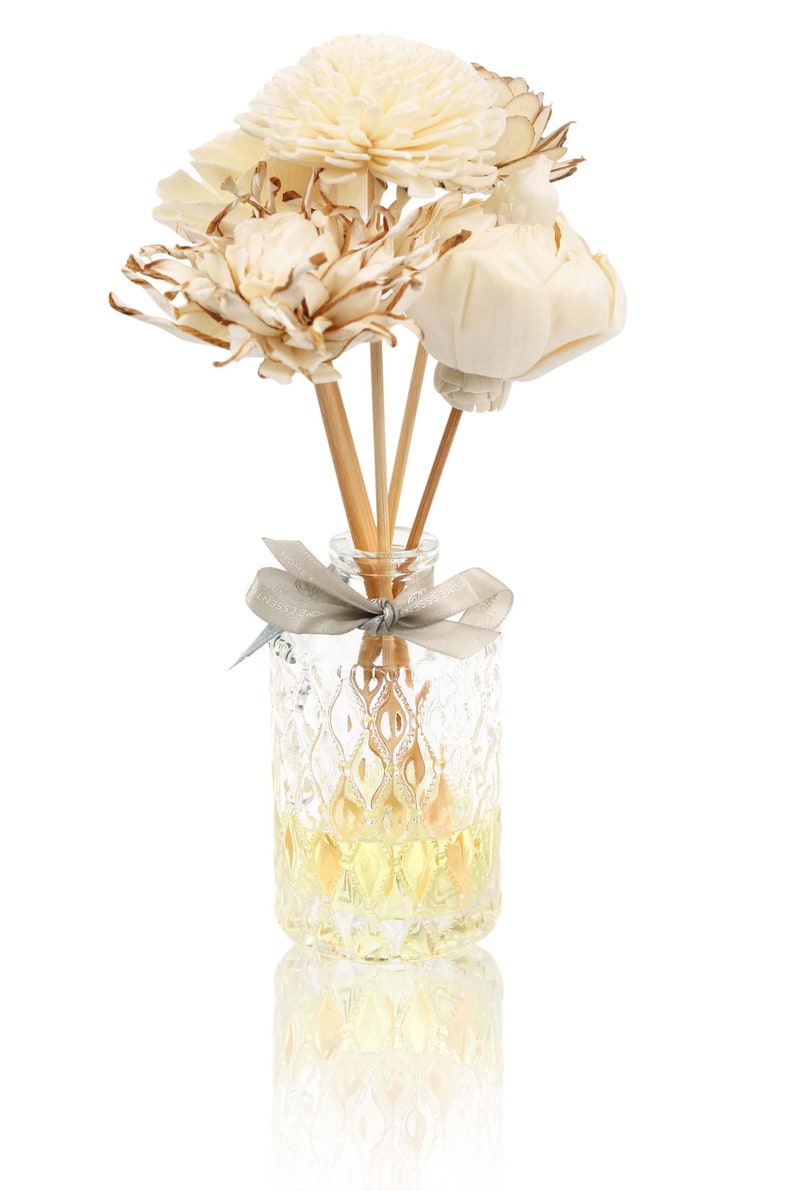 May include: A clear glass bottle with a decorative pattern filled with a yellow liquid and wooden sticks topped with dried white flowers.
