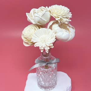 May include: A bouquet of white wooden flowers in a clear glass vase with a gray ribbon. The vase is sitting on a white rock-shaped base.
