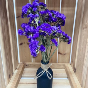 May include: A bouquet of dried purple statice flowers in a black vase with twine tied around the neck.