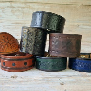 Puede incluir: Seis pulseras de cuero con diferentes diseños en relieve. Las pulseras están apiladas unas sobre otras. Las pulseras son de color marrón, negro, verde y azul.