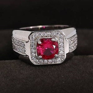 May include: A silver ring with a large, square-shaped, red gemstone surrounded by smaller, clear gemstones.