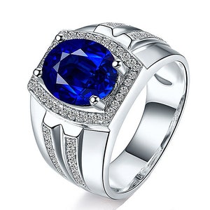 May include: A silver ring featuring a large oval blue gemstone encircled by smaller white gemstones. The ring has a textured band with an embossed design.