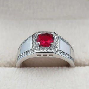May include: A silver ring with a large red gemstone surrounded by smaller white gemstones.