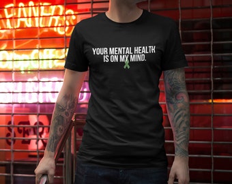 Puede incluir: Una camiseta negra con el texto "YOUR MENTAL HEALTH IS ON MY MIND." en letras blancas. Una cinta verde se encuentra debajo del texto.