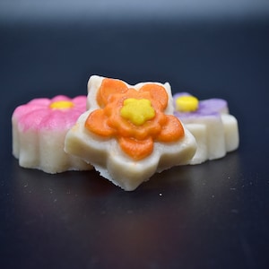 Könnte beinhalten: Drei weiße Zuckerkekse in Form von Blumen. Die Kekse sind mit rosa, orange und lila Zuckerguss verziert. Die Kekse liegen auf einer schwarzen Oberfläche.