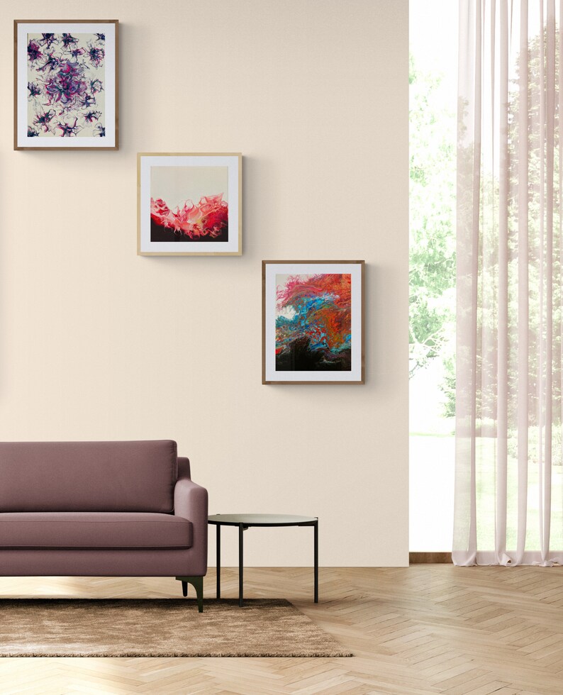 May include: Three framed abstract paintings with colourful swirls and splashes of colour hang on a beige wall above a brown sofa and a black side table.