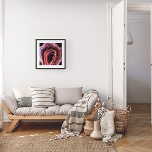 May include: A framed abstract painting with pink, red, blue, and black colors hangs on a white wall above a light gray couch with a striped throw blanket and pillows. The couch is in a living room with a wooden floor and a white door.
