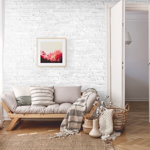 May include: A living room with a white brick wall, a light grey sofa, a wooden coffee table, and a framed abstract painting. The room has a white door and a white rug.