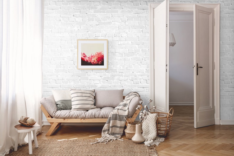 May include: A living room with a white brick wall, a light grey sofa, a wooden coffee table, and a framed abstract painting. The room has a white door and a white rug.