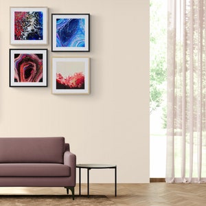 May include: A living room interior with a mauve sofa, a black side table, and a brown rug. Four framed abstract paintings hang on the wall behind the sofa. The paintings feature blue, red, and white colours.