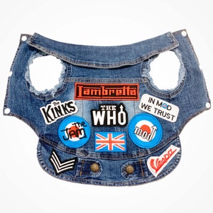 Può includere: Una giacca di jeans blu con varie toppe, tra cui "The Kinks", "The Jam", "The Who", "Lambretta", "In Mod We Trust", "Mod", "Vespa" e una bandiera Union Jack.