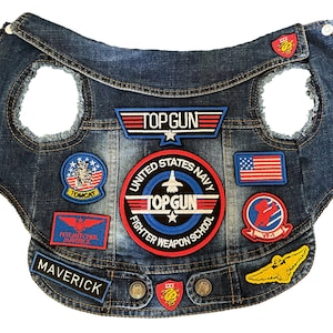 Può includere: Un giubbotto di jeans blu con toppe, tra cui "Top Gun", "United States Navy Fighter Weapon School", "Maverick", "Tomcat" e una bandiera americana.