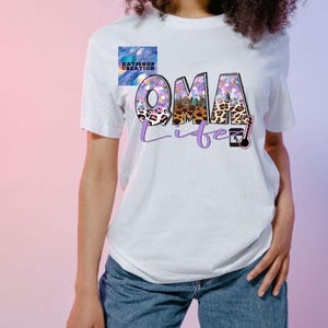 May include: White t-shirt with a purple and pink graphic that says "OMA life" with a leopard print design. The graphic also includes a small purple pill bottle with a white "Rx" on it.