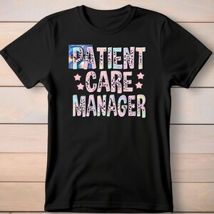 Op de afbeelding: Zwart t-shirt met de tekst "PATIENT CARE MANAGER" in een kleurrijk, patroonlettertype. De tekst bevat sterren en een mix van kleuren zoals blauw, roze en luipaardprint. Het shirt wordt gepresenteerd tegen een lichte houtnerf achtergrond.