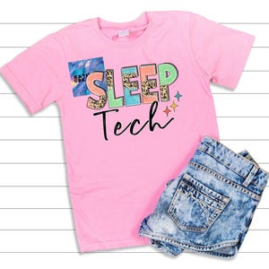Puede incluir: Una camiseta rosa con las palabras "SLEEP Tech" en letras coloridas y divertidas. La letra "E" de "SLEEP" tiene un diseño de estampado de leopardo. La camiseta se combina con pantalones cortos de mezclilla, creando un look casual.
