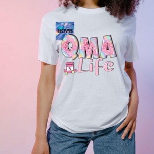 Puede incluir: Camiseta blanca con el texto "QMA Life" en un diseño pastel colorido. Las letras "QMA" tienen un efecto tie-dye, y la palabra "Life" es rosa. También hay un pequeño frasco de pastillas y un gráfico de pastillas.