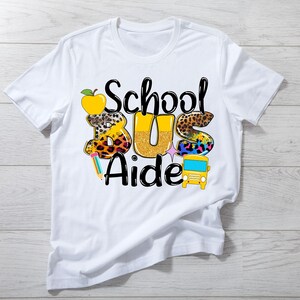 May include: White t-shirt with a graphic design that says "School Bus Aide" with a yellow school bus, an apple, and a pencil.