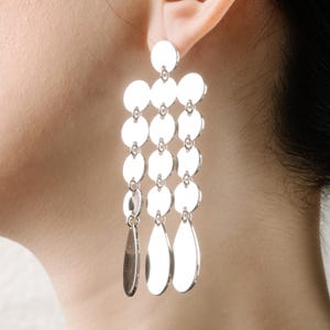 May include: Silver dangle earrings with multiple round and teardrop shaped charms.