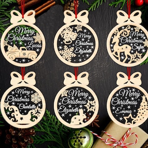 May include: Six wooden Christmas baubles with red ribbons. Each bauble is a circle with a bow at the top and a cutout design. The baubles have the words "Merry Christmas" and a name, such as Lucas or Emma.