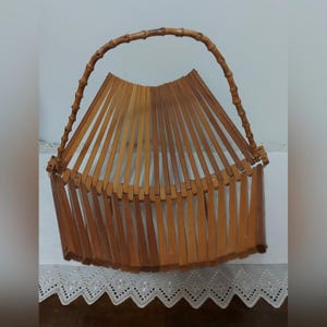 May include: A bamboo basket with a curved handle. The basket's body is made from vertical bamboo slats, radiating from a central point. The handle is made of thicker, curved bamboo. The basket is a natural brown colour.