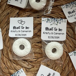 May include: White mint candies in clear plastic packaging, each with the word "ZERO" embossed on them. The candies are paired with small white tags that read "Mint to be" and the names Kristy & Cameron, with the date 12/28/2024.