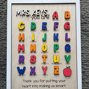May include: A wooden framed sign with the words "MRS. KEYS, you are" and a colorful alphabet with a positive word for each letter. The sign also includes the text "Thank you for putting your heart into making us smart."
