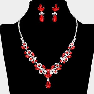 May include: A silver necklace and earrings set with red crystal accents. The necklace features a teardrop pendant and a floral design.