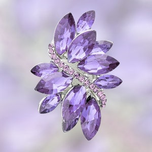 May include: A purple rhinestone brooch in the shape of a stylized flower with a silver metal base.