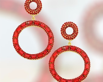 May include: A pair of gold hoop earrings with red crystal accents. The earrings are large and have a circular design.