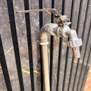 May include: A stainless steel outdoor tap with a long, flat lever handle and a ribbed hose nozzle attachment. The metal fixture features a 304 grade stamp on the valve body and is connected to a vertical pipe, showcasing a brushed metallic finish.