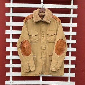May include: A tan jacket with a brown faux fur collar and leather elbow patches. The jacket has a button closure and two flap pockets.